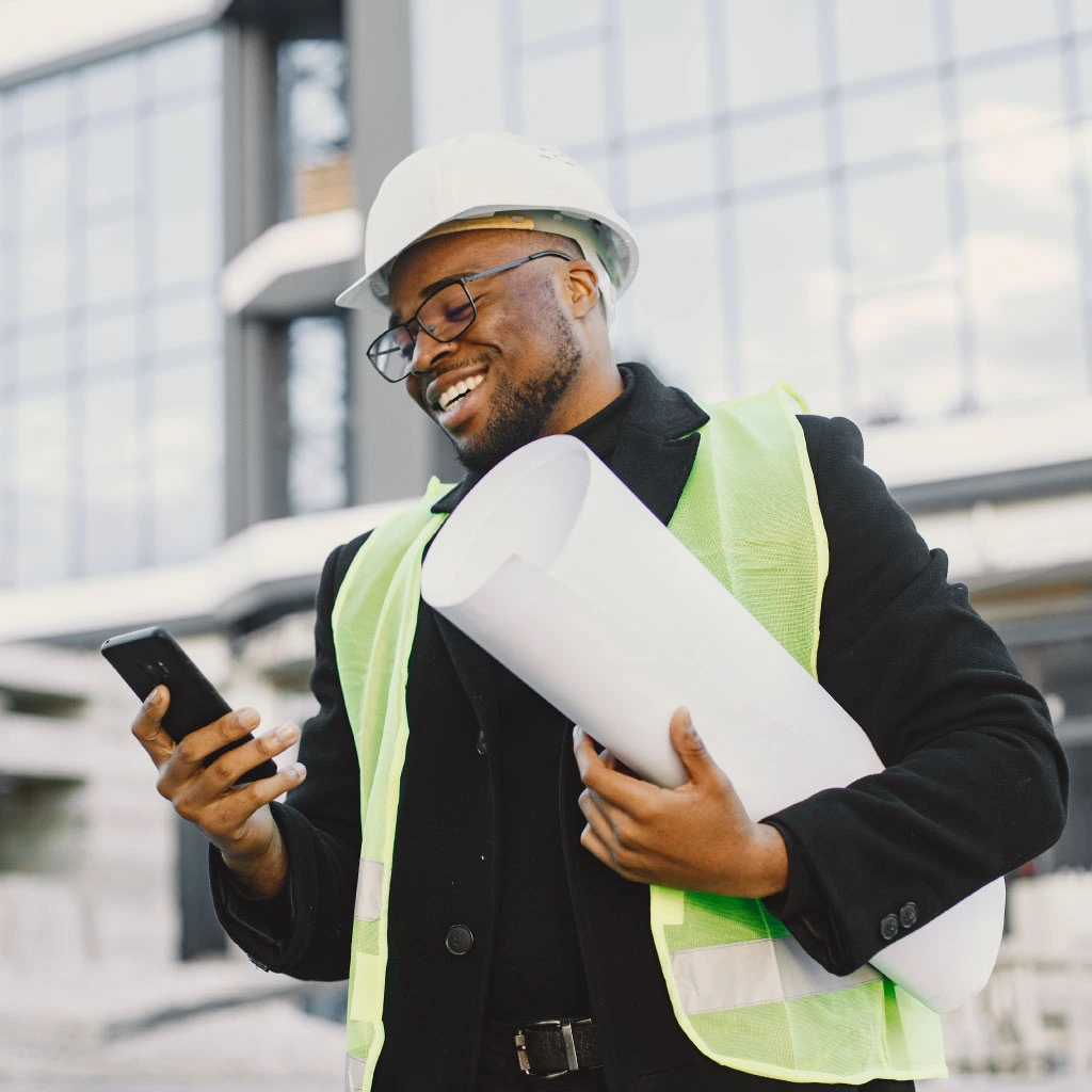 Young Black man standing outside a modern glass building holding a blueprint.